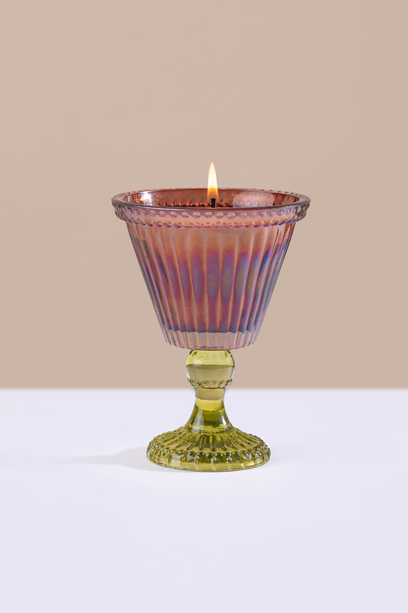 brown glass candle holder with a lit candle on a beige background